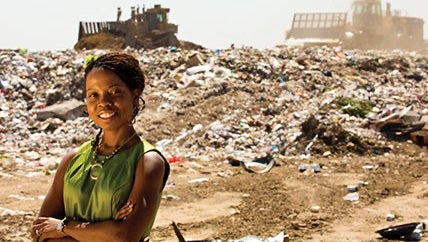 A woman poses in front of a landfill with bull dozers in the background.