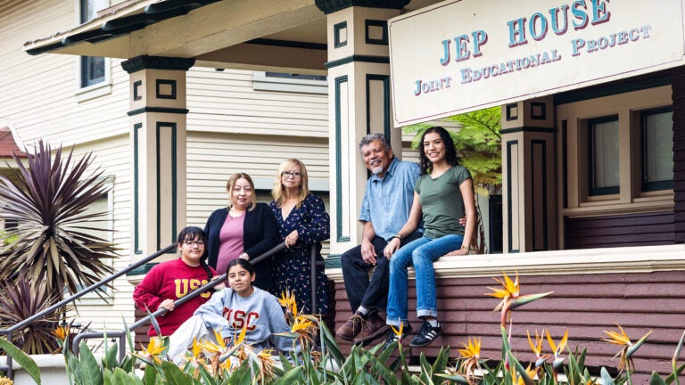 Multigeneration families sit and stand on the steps and porch rail of USC’s JEP House