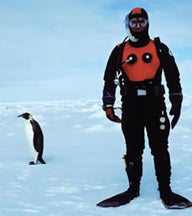 Donal Manahan suited for a polar dive, a penguin on the ice behind him