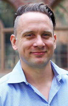 Portrait of neuroscientist Andrew Hires wearing a blue gingham collared button-down shirt and smiling slightly