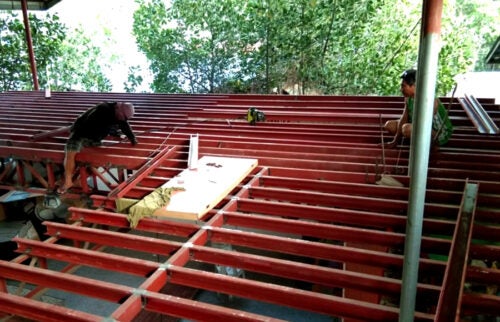 Filipino construction workers build a roof with red rafters and joists.