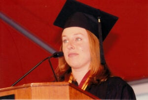 A photo of Katie Trefz speaking at a podium in graduation regalia.