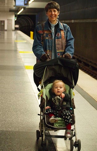A photo of a woman pushing a stroller with a toddler pointing at the camera.