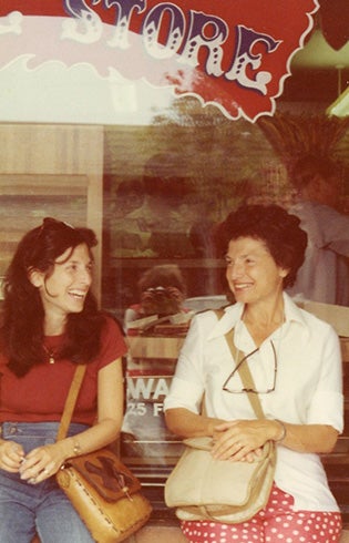 A faded photo of smiling two women sitting in front of a storefront.