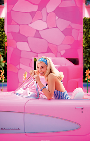 Actor Margot Robbie portraying Barbie sits in a pink car in front of a pink wall