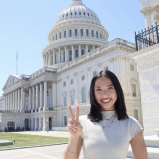 A woman makes a fight on hand symbol in front of the U.S. Capitol Building.