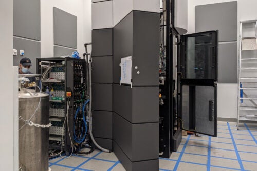 A technician adjusts equipment in a lab with machinery and server racks