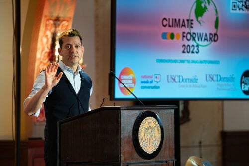 A person speaks at a podium with a screen in the back displaying Climate Forward 2023 slide