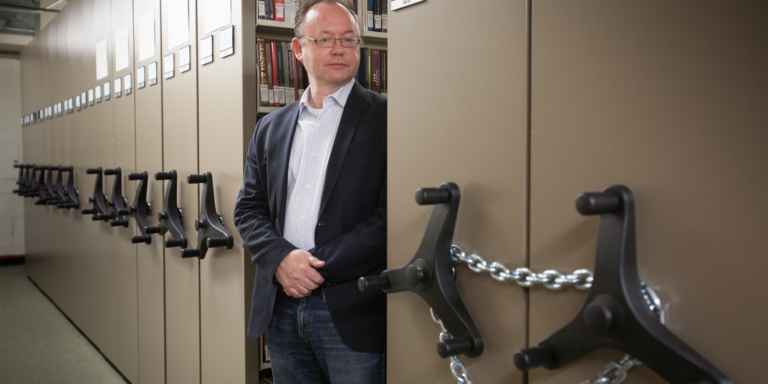 Wolf Gruner stands between shelves of a book archive.