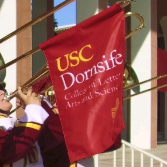 Marching band tronbone player with a USC Dornsife banner.