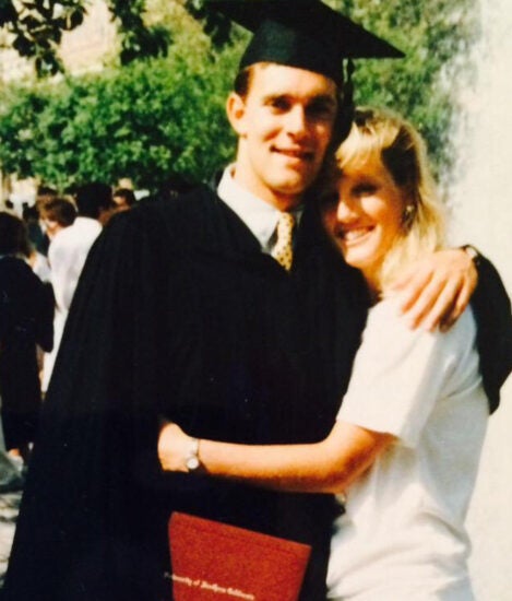 Randy Hetrick stands in graduation regalia with arm around a young woman hugging him