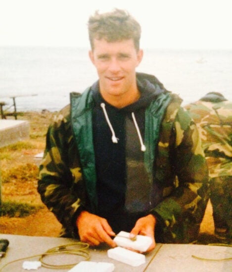 Young Randy Hetrick wears camouflage rain gear and a grey hoody on a rainy day