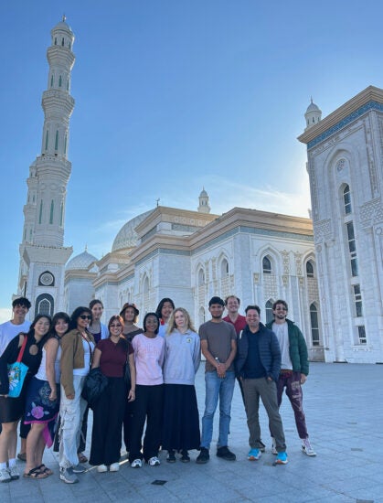 Students and their instructor stand in front of a white mosque with ornate gold