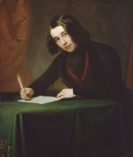 A young, androgynous person sits at a table holding a feathered quill over a piece of paper while looking at the viewer