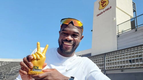 Rai Benjamin on USC’s track field smiles and holds a gold statuette of the Fight On! Gesture