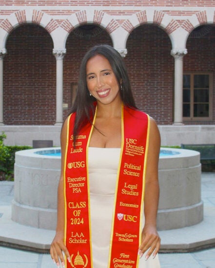 Sophia Perez displays her graduation sash while standing in front of a fountain in USC’s campus