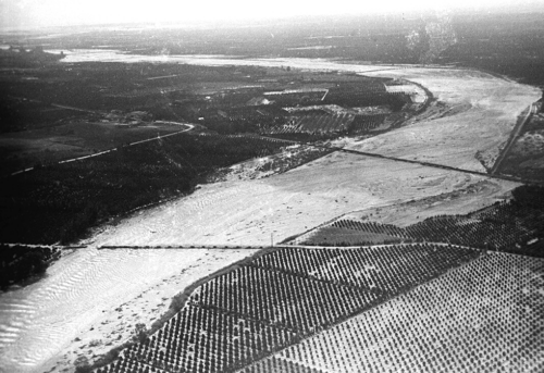 Black-and-white aerial photo of flooded crops and neighborhood