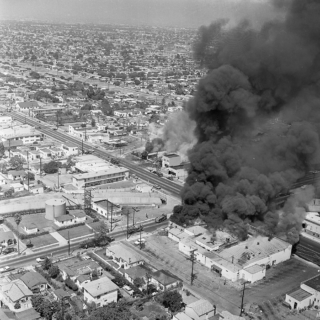 Smoke billows from a building in this black-and-white aerial photo of Los Angeles