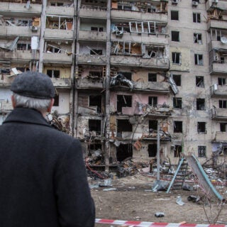 Man in coat and hat, back to camera, views remains of bombed tenement building in Kyiv, Ukraine