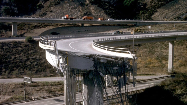 Metal infrastructure hangs from a broken freeway overpass