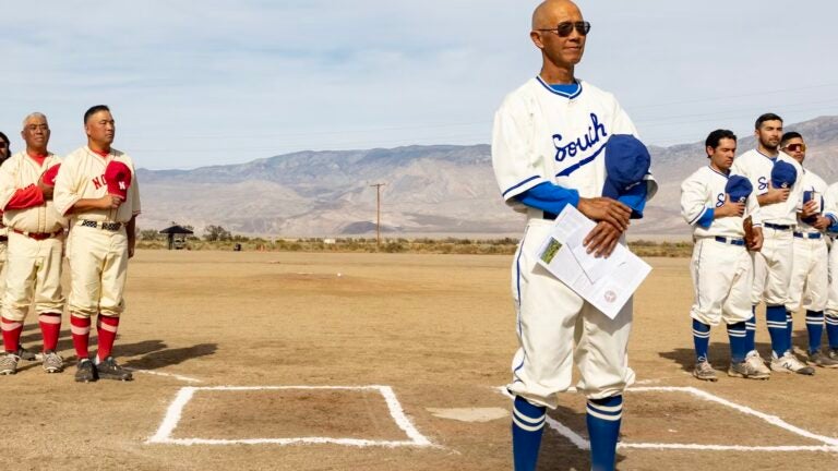Two teams in uniform stand on baseball field