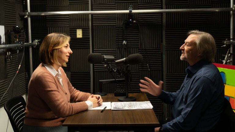 Shushan Karapetian and Peter Cowe sit opposite one another in a podcast studio