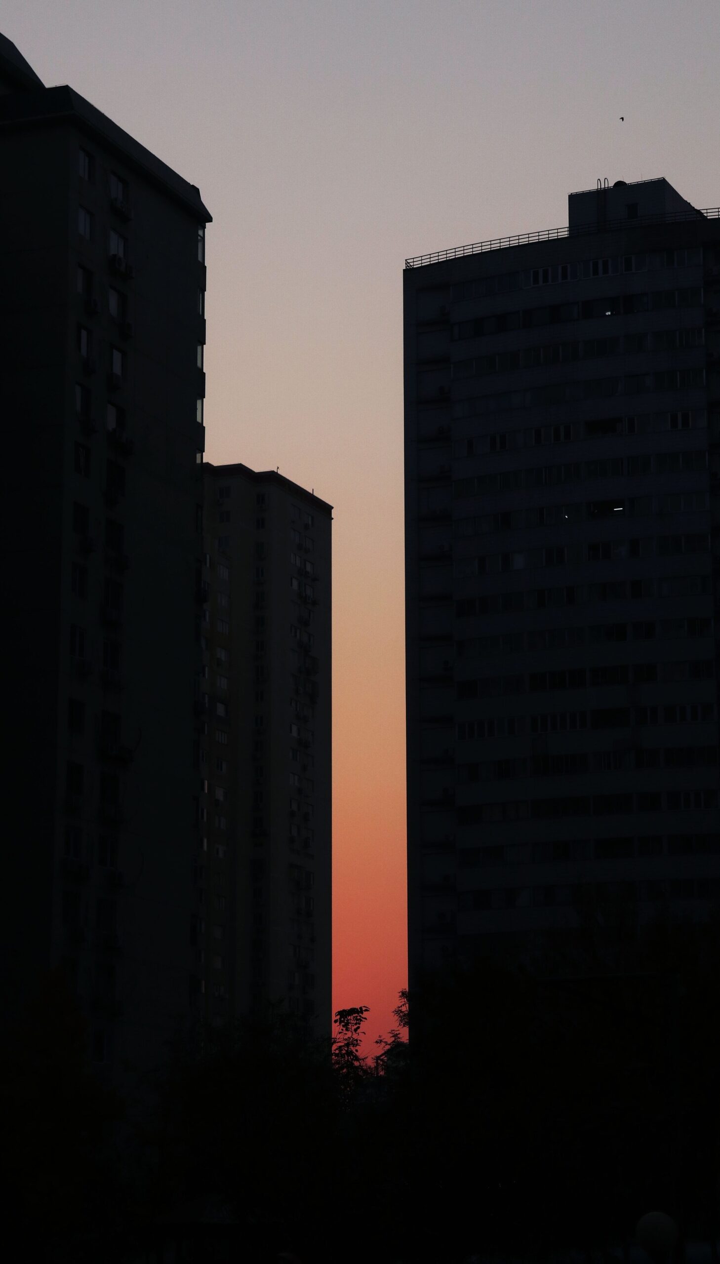 Silhouette of two buildings; in between the gap is the sunset