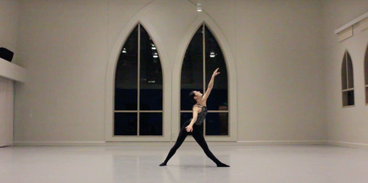 Photo of a dancer in a pose with her feet apart and her arm raised