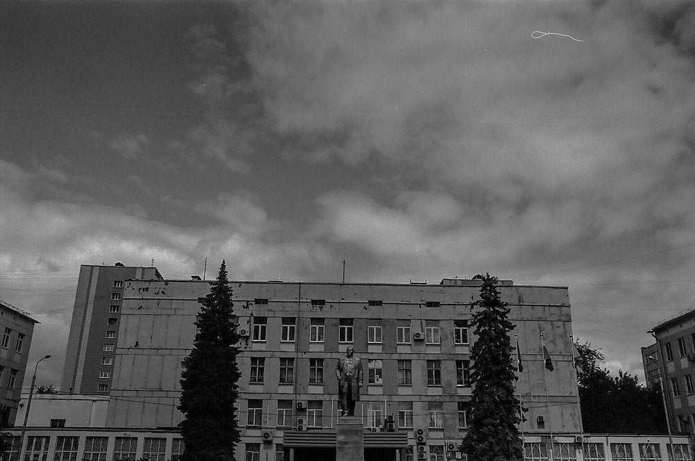 Black and white photo of building, sky, two trees, and a statue