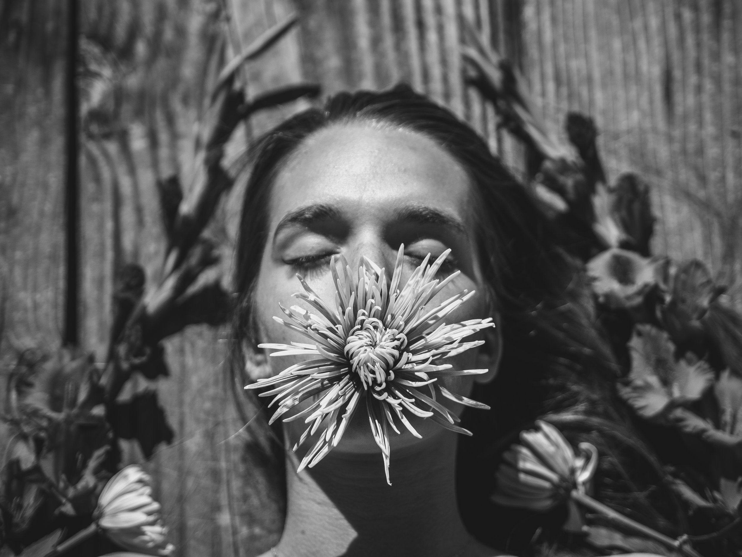 Black-and-white photo of woman lying down, with a large flower on her face over her mouth and nose.