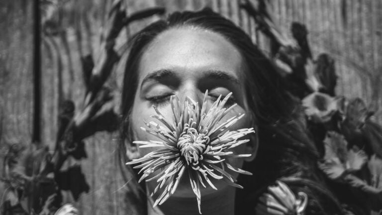 Black-and-white photo of woman lying down, with a large flower on her face over her mouth and nose.