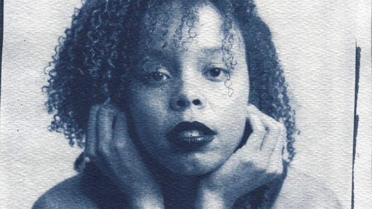 Young woman with curly hair and dark lipstick gazes at the camera, resting her head in her hands