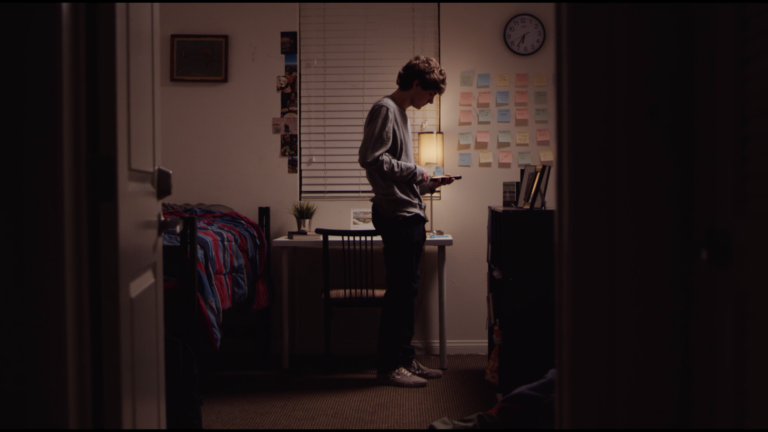A man stands in a bedroom holding a framed photo(?).