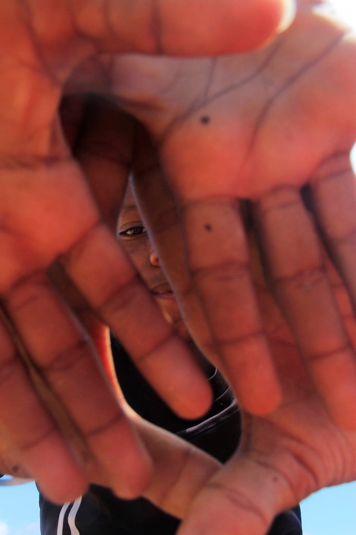 Image of a child with their hands obscuring the camera; their eye is visible.
