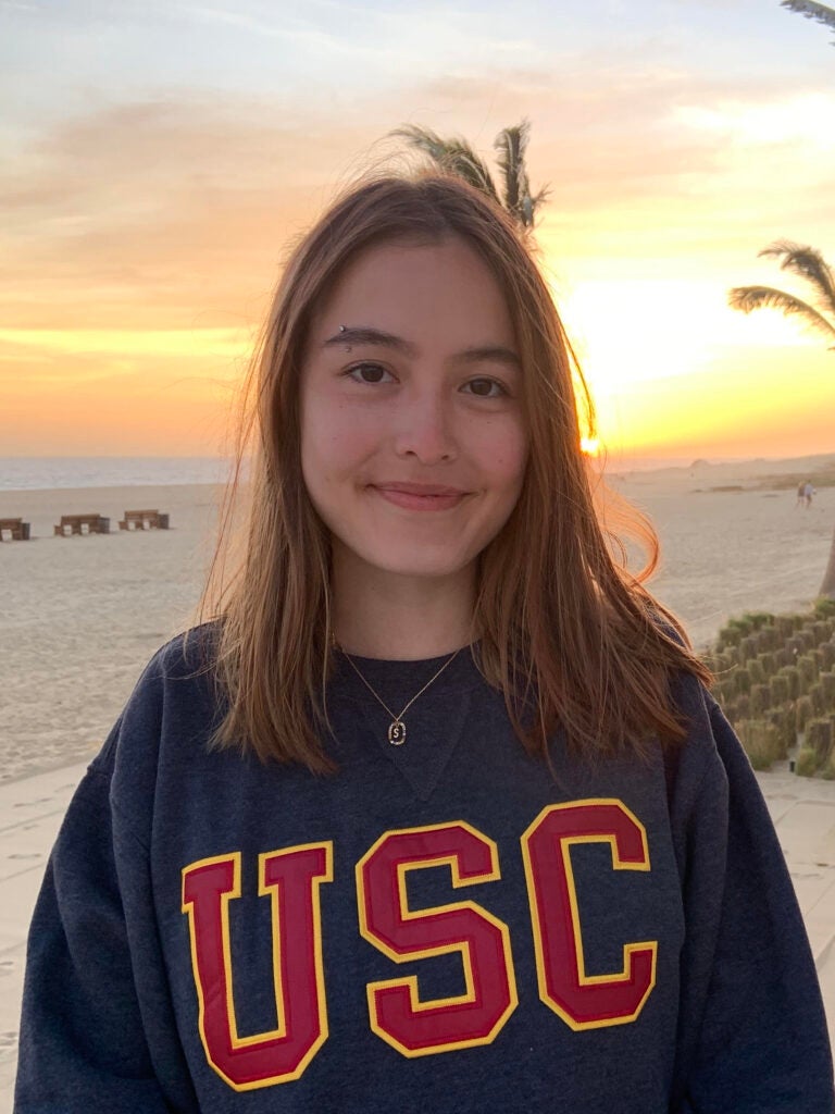 Person facing the camera and smiling with closed mouth, beach sunset with palm trees in the background, centered red and gold 