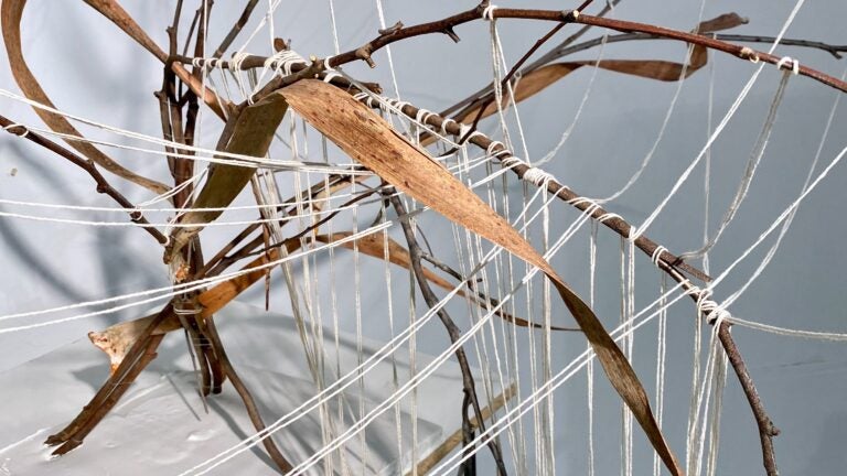 Dried branches and leaves are bent, connected, and bound by twine. The twine wraps around and hangs from the branches.
