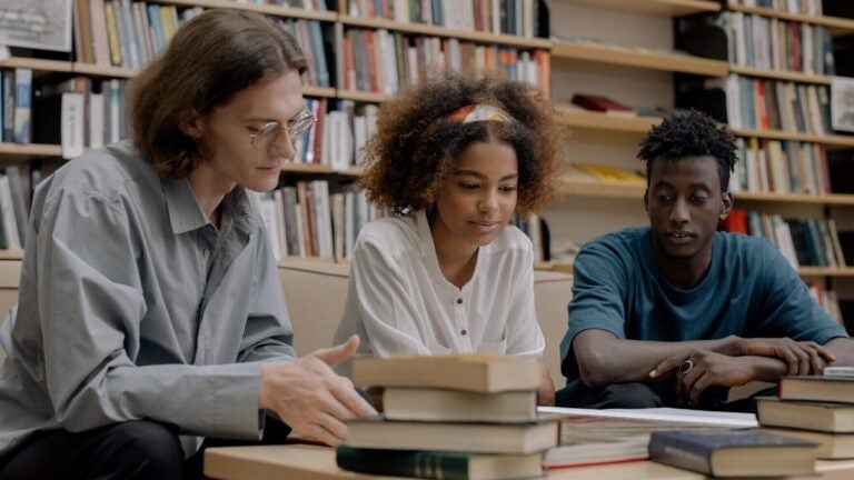 3 students sitting in the library reading books