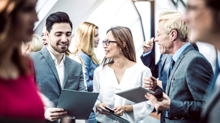 Group of people talking but especially, a man and woman is standing looking at their tablet and discussing a topic