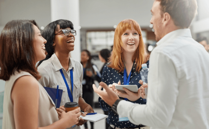 3 females are networking with a male who works in an industry that we would like to work at, and they're listening to his experiences at a networking event