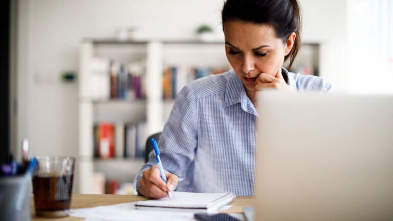 Photo of a female student contemplating hard at her desk while writing in her notebook