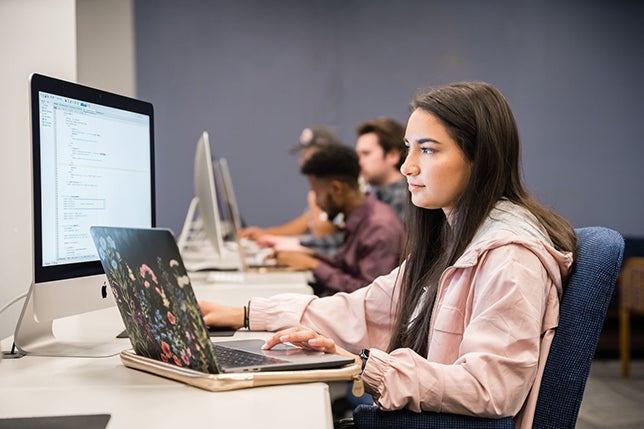female student on a desktop and her laptop working on her work