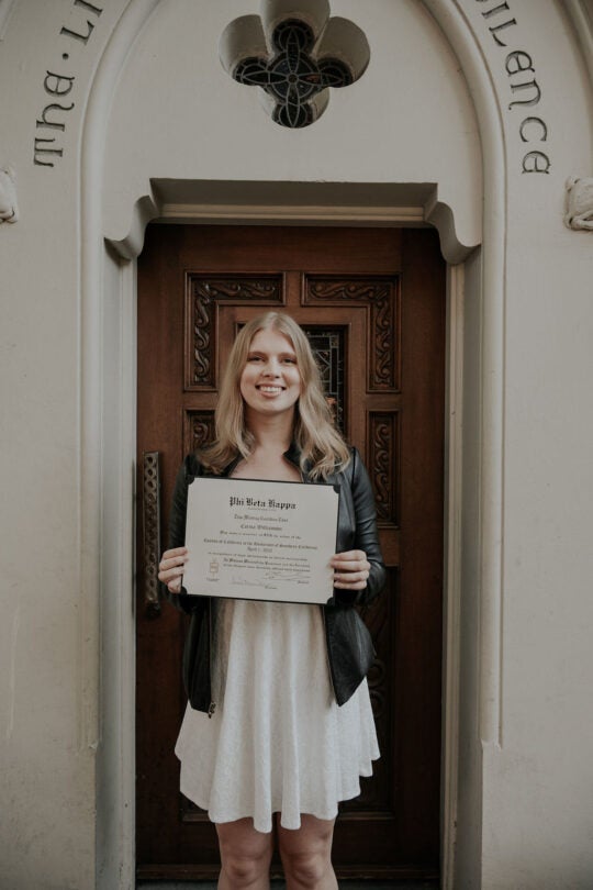 Inductee smiling and holding membership certificate, standing in front of doorway.