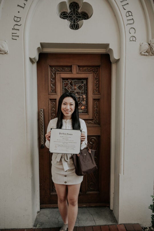 Inductee smiling and holding membership certificate, standing in front of doorway.