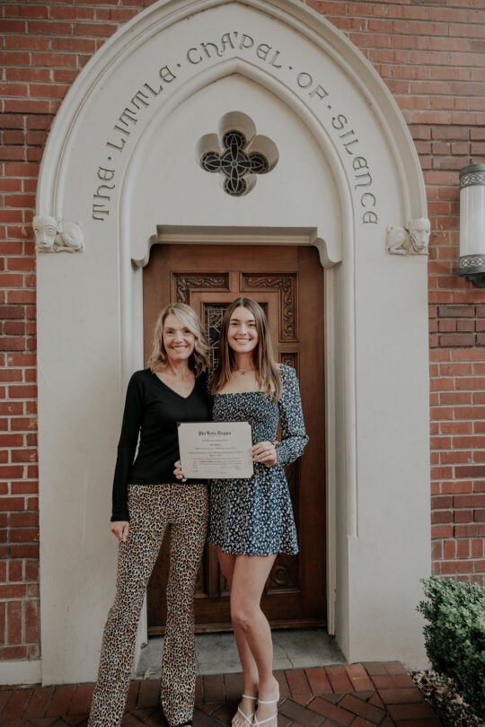 Inductee holding certificate and standing with guest in front of the doorway to the Little Chapel of Silence. Both are smiling.