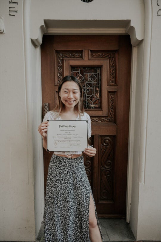 Inductee standing at doorway, holding membership certificate, and smiling.