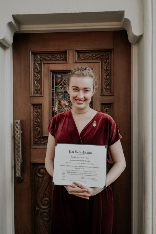 Inductee standing at doorway, holding membership certificate and smiling.