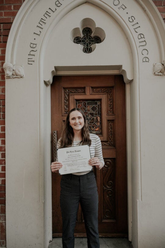 Inductee standing at doorway to the Little Chapel of Silence, holding membership certificate and smiling.