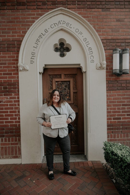 Inductee standing at doorway of the Little Chapel of Little Chapel of Silence, smiling and holding membership certificate.