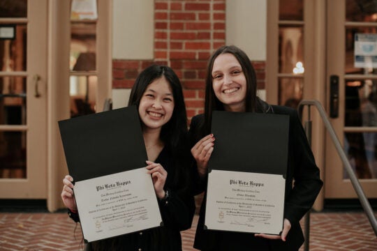 Two inductees, smiling, holding membership certificates outside of Town and Gown.