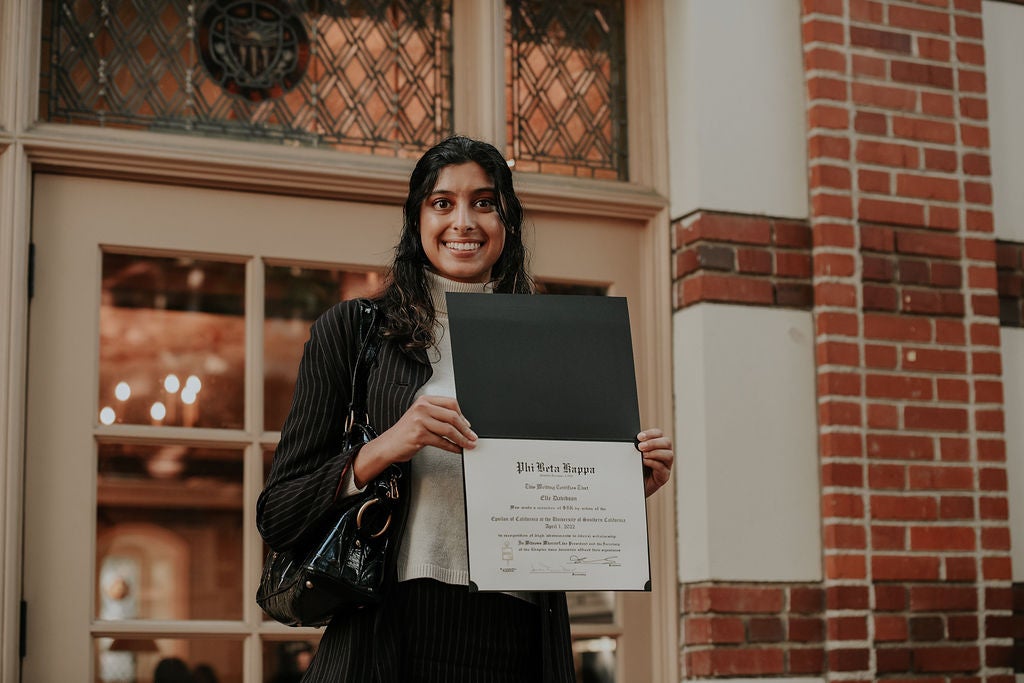Inductee smiling and holding membership certificate. Standing outside of Town and Gown.